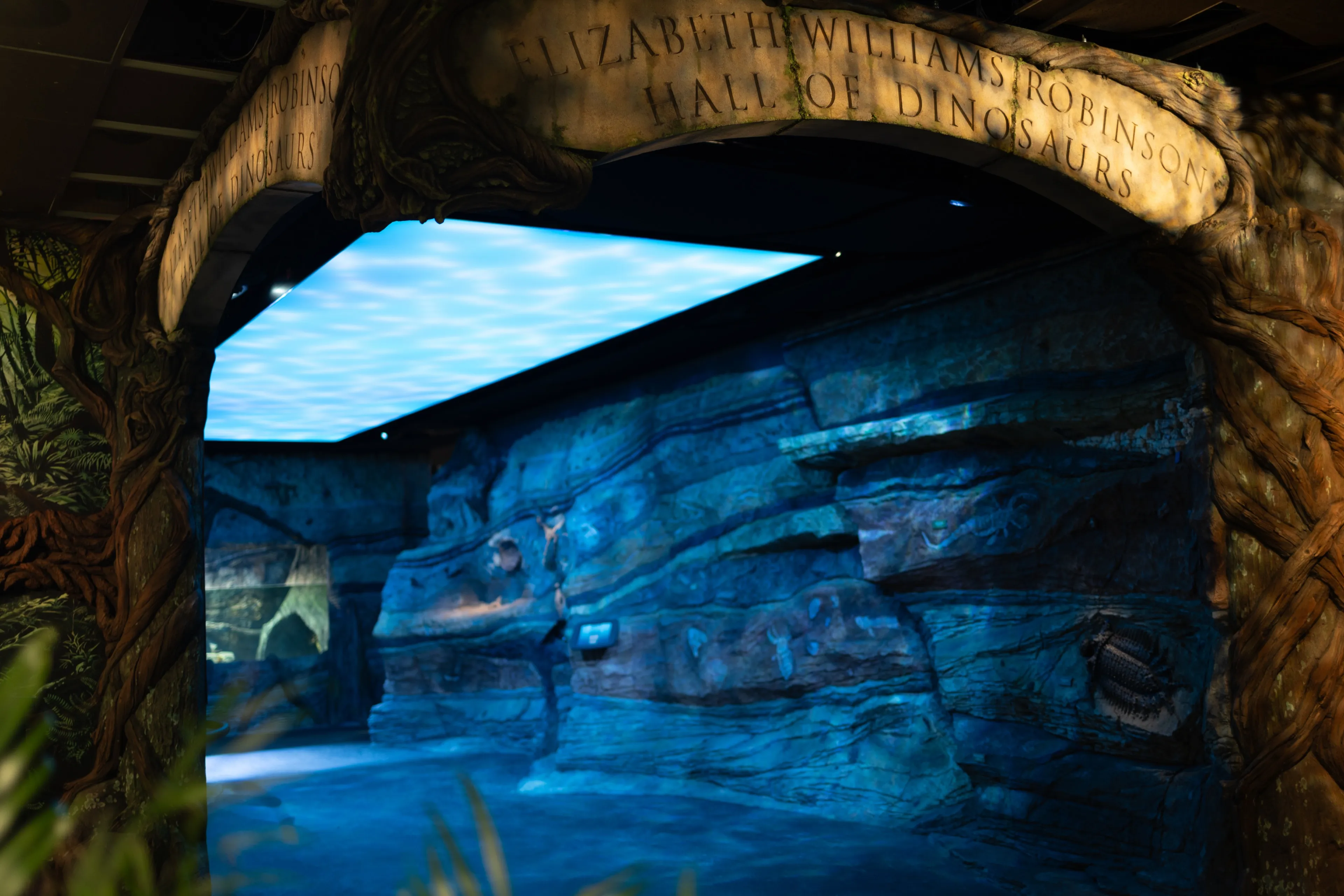The carved entrance arch of the Hall of Dinosaurs, the blue-lit riverbed passage beyond it